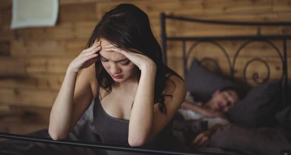 upset woman sitting bed while man sleeping background